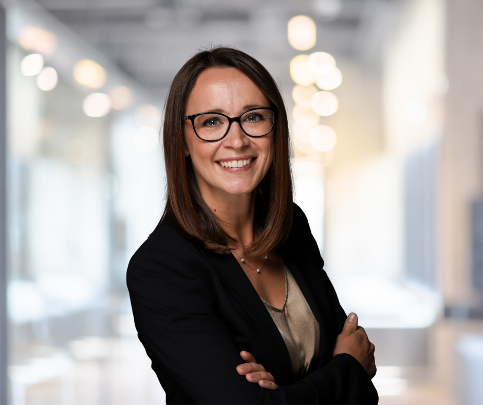 Professionelle Frau mit Brille und Business-Outfit lächelt selbstbewusst in einem modernen Büroambiente, ideal für Beiträge über Karriere, Networking und persönliche Entwicklung.