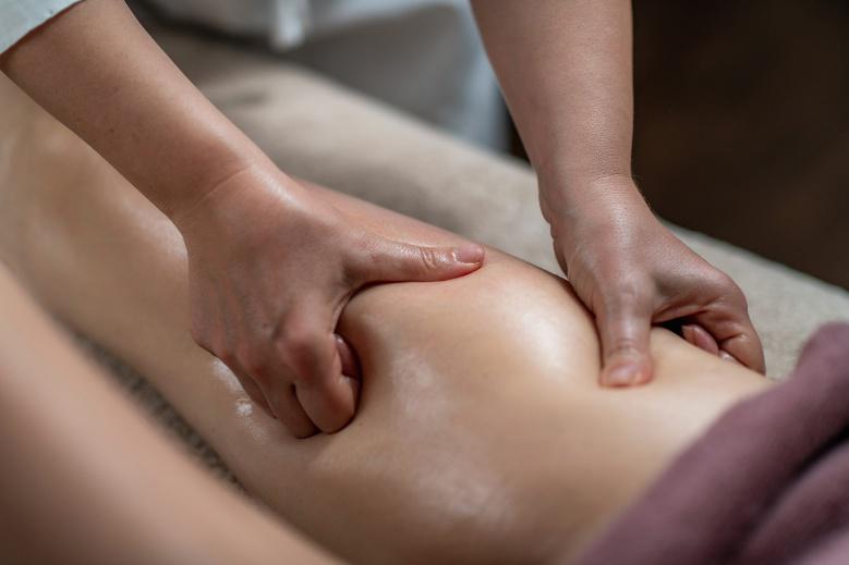 Massagebehandlung an einem Oberschenkel, bei der eine Therapeutin mit beiden Händen eine entspannende Technik anwendet, um Verspannungen zu lösen und die Durchblutung zu fördern.