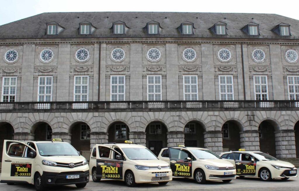 Flotte von Taxis vor einem historischen Gebäude mit eleganten Fenstern und einer steinernen Fassade, ideal für Stadtfahrten und Transfers.