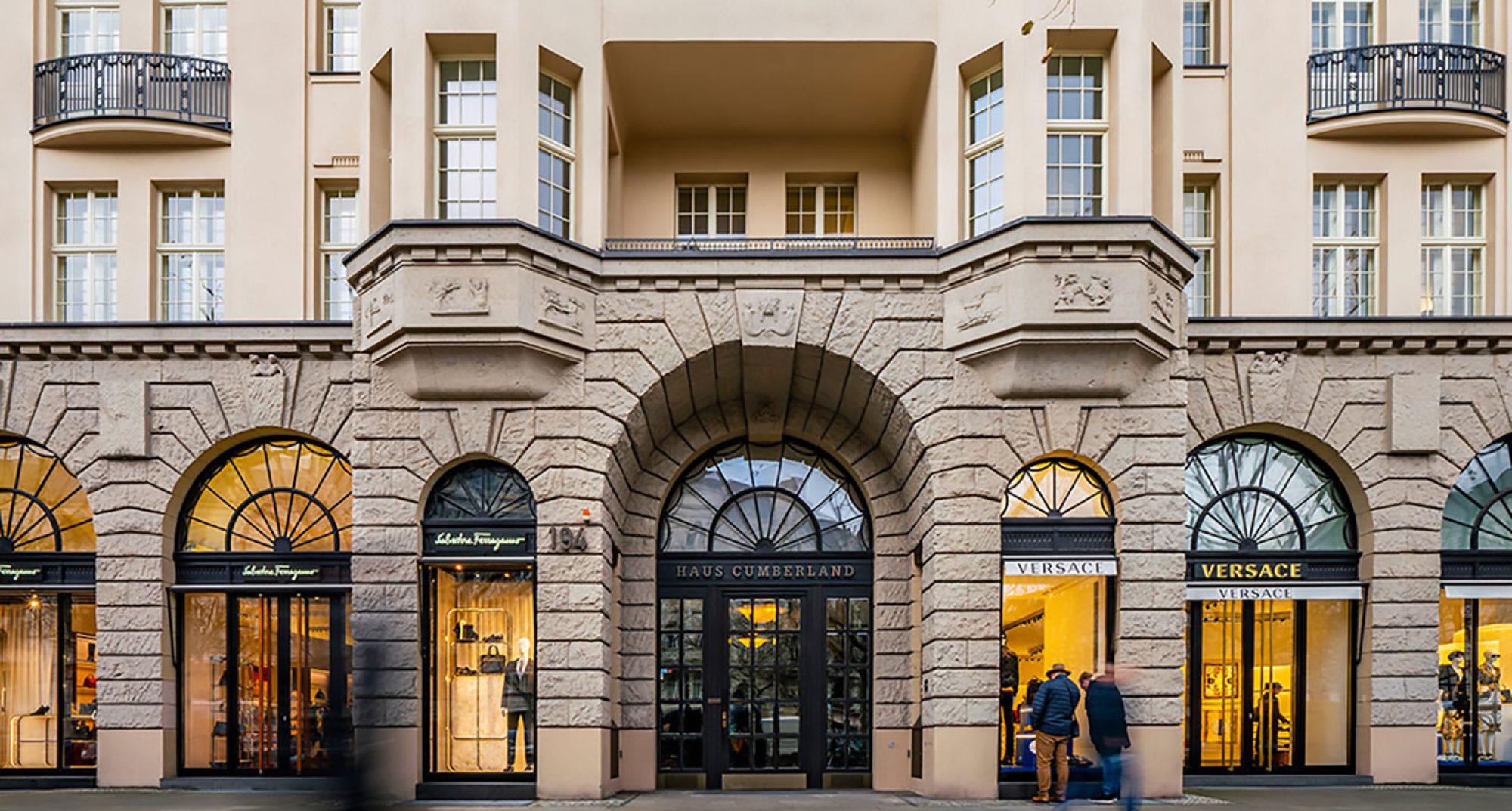Eingang zum Haus Cumberland mit eleganten Schaufenstern von Salvatore Ferragamo und Versace, umgeben von einer stilvollen Architektur in einer belebten Einkaufsstraße.