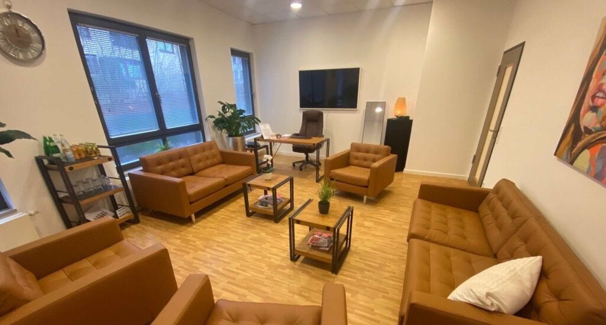 Moderner Wartebereich mit braunen Sofas und Sesseln, stilvoll eingerichtet mit Pflanzen und einem großen Flachbildfernseher, geeignet für Kontakt und Meetings.