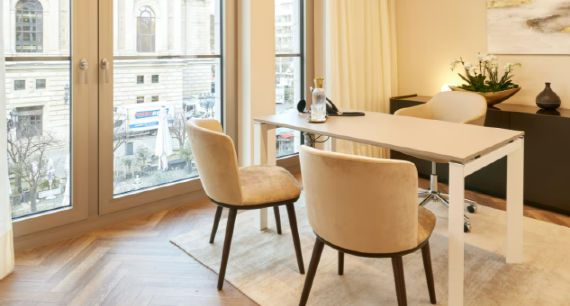 Modernes Büro mit eleganter Einrichtung und großem Fenster mit Blick auf ein historisches Gebäude, ideal für Kontaktgespräche.